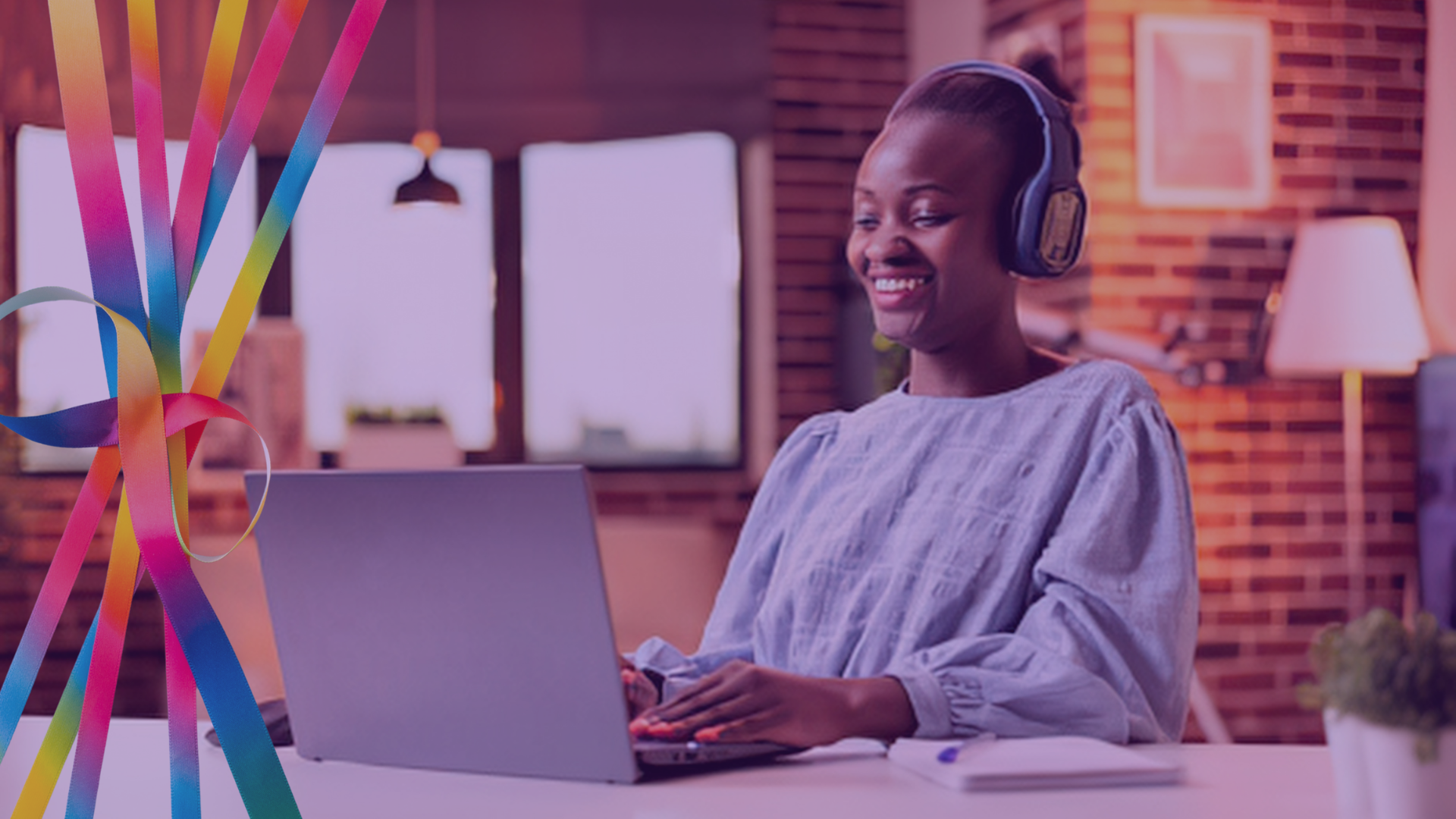 An African-American woman smiles while working at a laptop and wearing headphones. Over the image are multi-colored ribbons in the shape of an infinity symbol.
